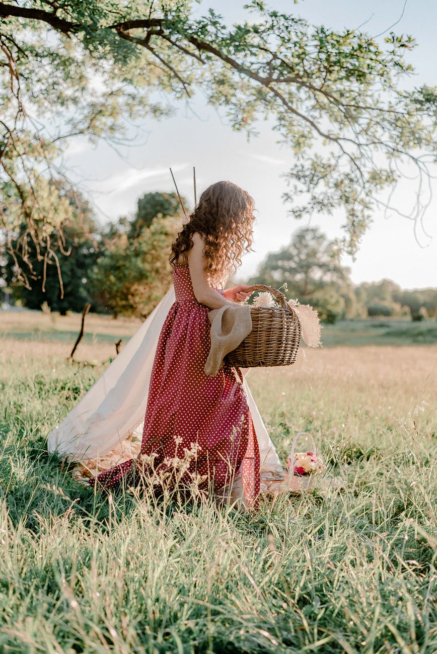 woman in red and white polka dot dress holding brown woven basket on green grass field